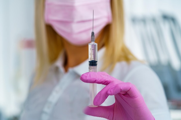 Nurse hand in pink gloves holding syringe with vaccine for a baby or adult Medicine and drug concept