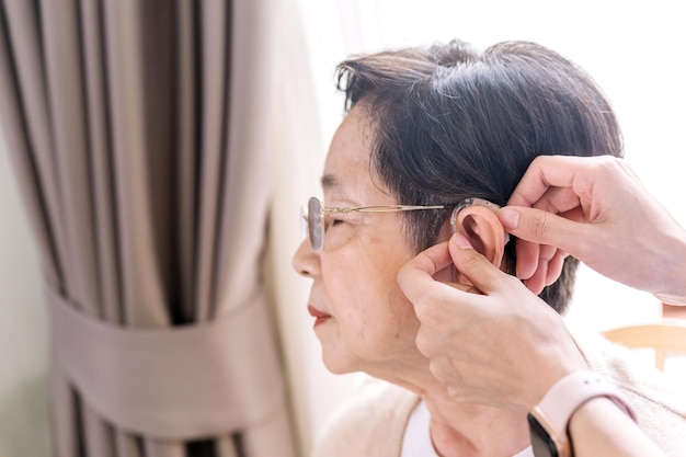 The nurse hands put the hearing aid on the senior woman ear The device increases louder sounds and then sends them to the ear through a speaker Caregiver visit Home health care and nursing home