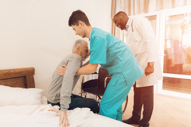 The nurse helps the elderly man to get out of bed.