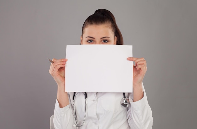 Nurse is hidding her face with a paper against of grey background