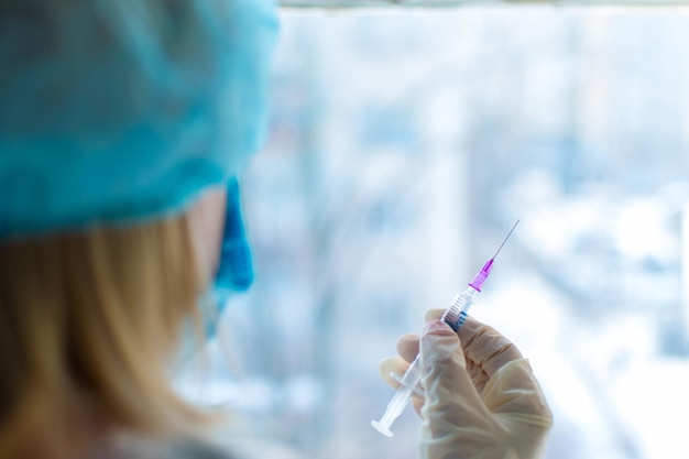 A nurse is holding a syringe with a vaccine on a light background