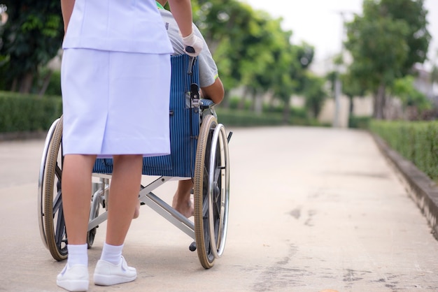 A nurse is pushing a wheelchair to a patient in the park