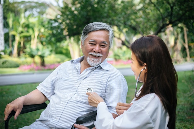 Nurse looking at elderly patient in a wheelchair. Doctor talking to old disabled 