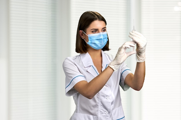 Nurse in medical mask looking at syringe