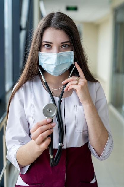 Nurse in overalls with mask on her face and stethoscope is smiling beautifully in the hospital