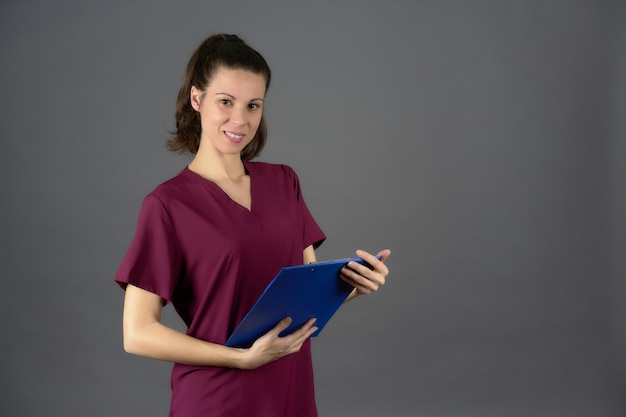 Nurse purple uniform looking into camera with medical report on clipboard on a gray background