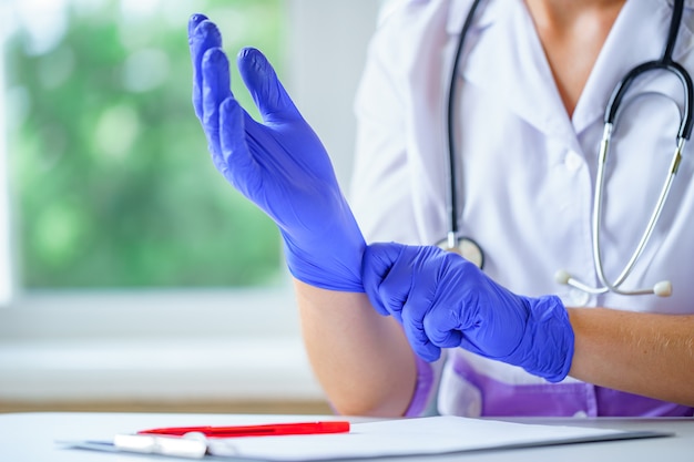 Nurse puts on blue rubber medical gloves for medical examination of a patient in a clinic