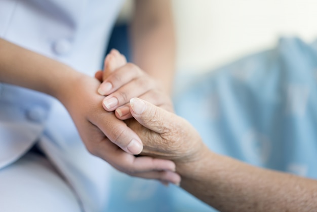 Nurse sitting on a hospital bed next to an older woman helping hands 