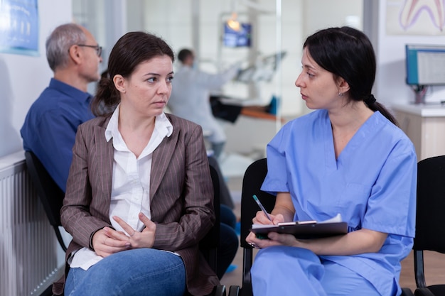 Nurse taking notes on clipboard about patient dental problems waiting for orthodontist sitting on ch...