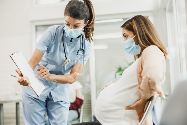 Nurse talking to worried pregnant woman before covid-19 vaccine at hospital waiting room.