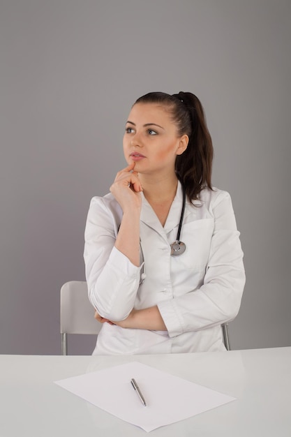 Nurse in white robe and black glasses and stethoscope is checking her report and thinking about it