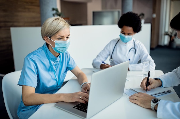 Nurse with protective face mask working on laptop at medical clinic