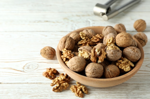 Nutcracker and bowl of walnuts on white wooden background