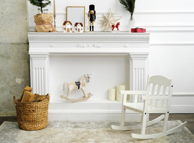 A nutcracker candles in the form of houses a rocking horse and a natural Christmas tree stand on the fireplace Rocking chair stands next to the fireplace