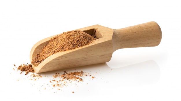 Nutmeg powder in wood scoop on white