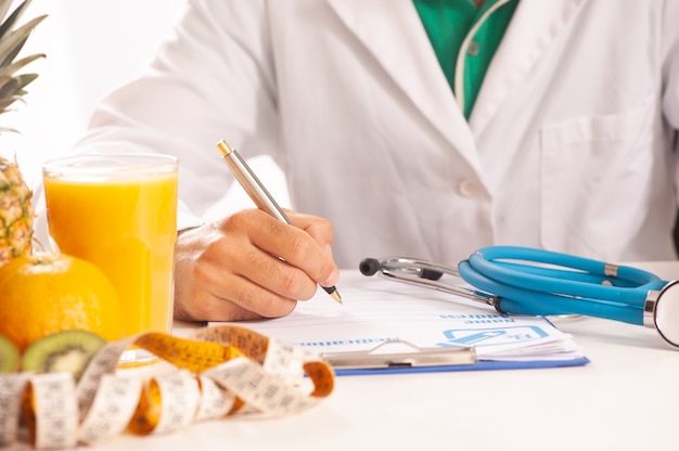 Nutrionist writing a diet plan on table with healthy fruits close up