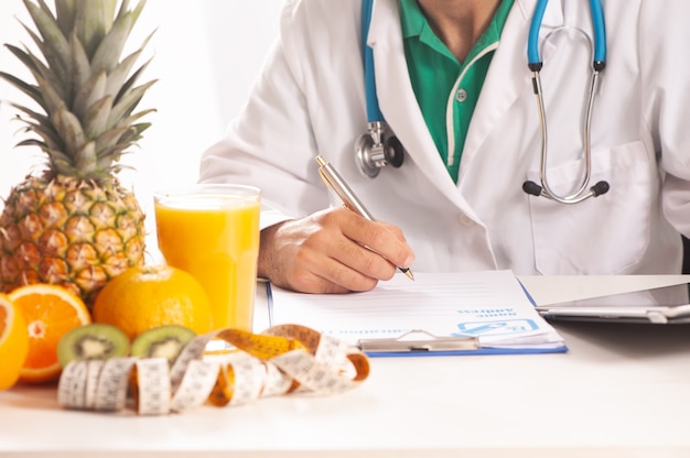 Nutrionist writing a diet plan on table with healthy fruits close up