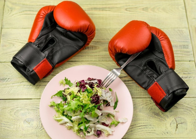 Photo nutrition for sports healthy active way of life vegetarian salad of fresh vegetables and boxing gloves on a wooden background