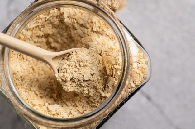 Nutritional yeast in flakes with a wooden spon and a glass jar on grey background