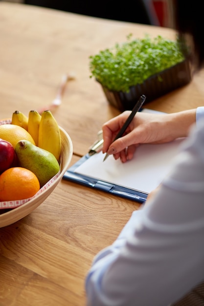 Nutritionist, dietitian woman writing a diet plan, with healthy vegetables and fruits, healthcare and diet concept. Female nutritionist with fruits working at her desk, workplace