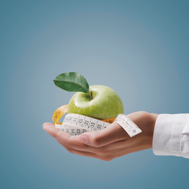 Nutritionist holding a tape measure and an apple fitness and diet plan concept