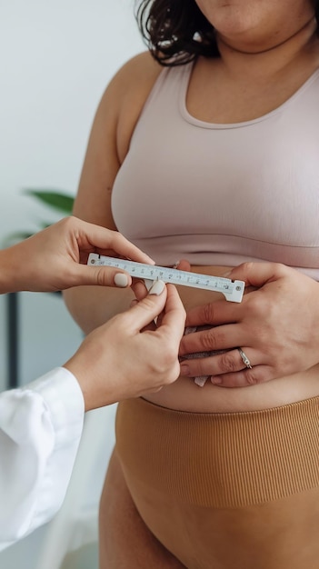 Nutritionist measuring overweight woman39s body fat layer with caliper in clinic closeup