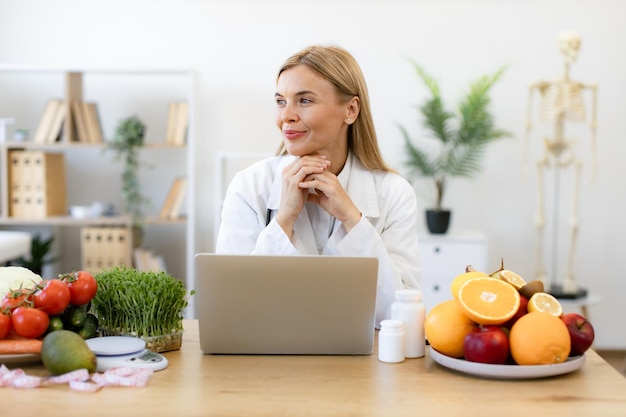 Photo nutritionist working on laptop and writing diet plan for patient