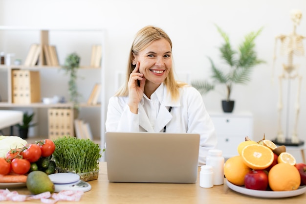 Photo nutritionist working on laptop and writing diet plan for patient