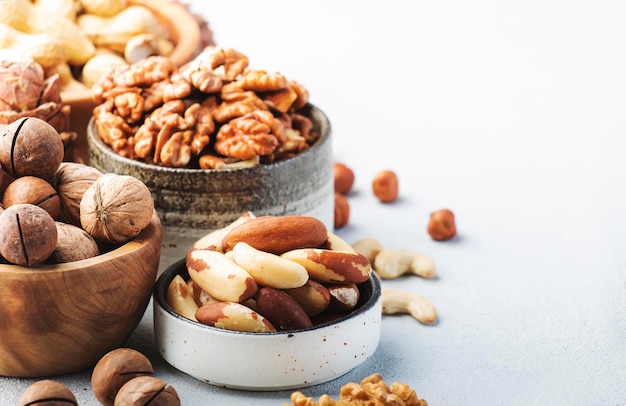 Nuts in bowls Cashews hazelnuts walnuts pecans almonds and other Healthy food snack mix on gray table background copy space