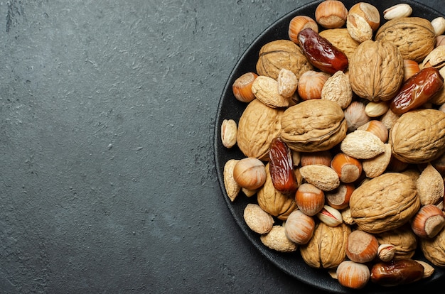 Nuts and dates in a plate on a dark concrete background. Source of vegetable protein and vitamins.