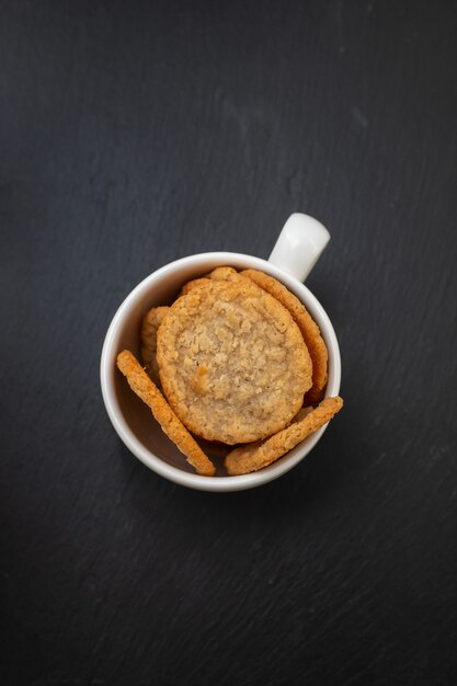 Oat cookies in the white cup on black ceramic table