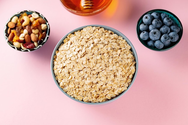 Oat flakes, blueberries, nuts and honey on a pink background. Dry oatmeal and ingredients for making a diet breakfast. Healthy breakfast concept. Top view