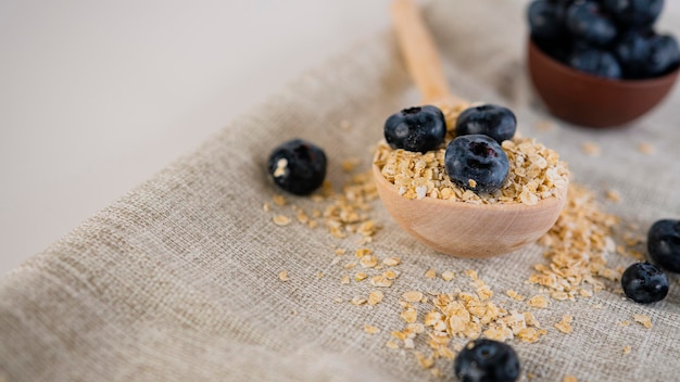 Oat flakes in large wooden spoon with blueberry on napkin on white background