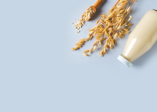 Oat milk in glass bottle with flakes and spike or ears of grain on blue background