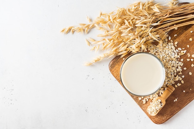 Oat milk in glass with flakes and spike or ears of grain on white background