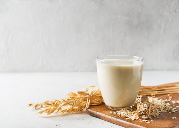 Oat milk in glass with flakes and spike or ears of grain on white background