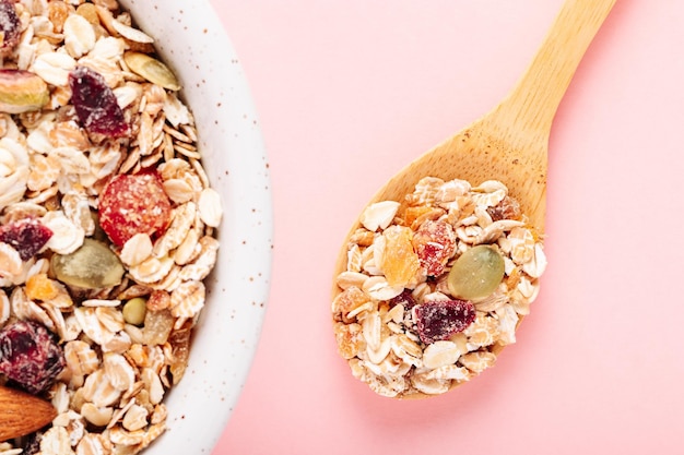 Oat muesli with nuts dried berries and seeds on a pink background closeup