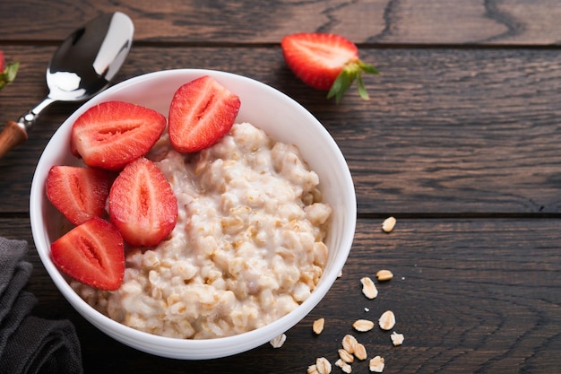 Oatmeal Bowl of oatmeal porridge with strawberry almond and milk on old wooden dark table background Top view in flat lay style Natural ingredients Hot and healthy breakfast and diet food