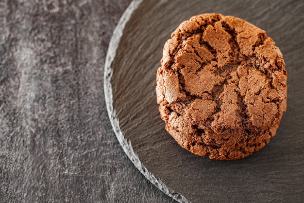 Oatmeal cookies made of chocolate brown dough folded into stack on slate stone plate round dark background selective focus