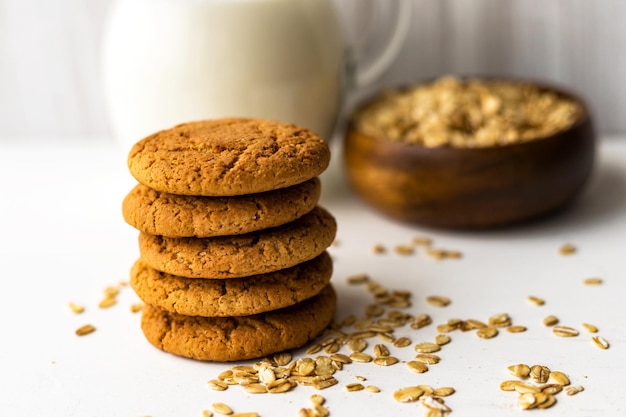 oatmeal cookies and oat cereal flakes bowl on white table on milk glass jug background