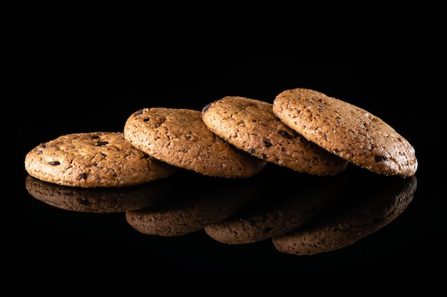 Oatmeal cookies with chocolate chips are isolated on a black background with a reflection Lots of brown round homemade cookies lying on a reflective surface closeup