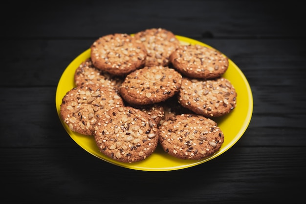 Oatmeal cookies with seeds and sesame seeds on a yellow plate on a black wooden background