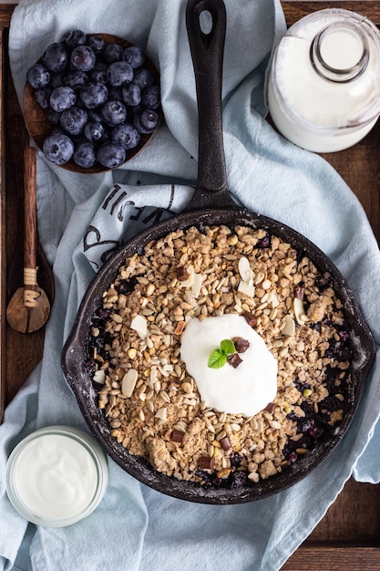 Oatmeal crumble in cast iron pan with fresh blueberry and natural yogurt. Healthy food concept. 