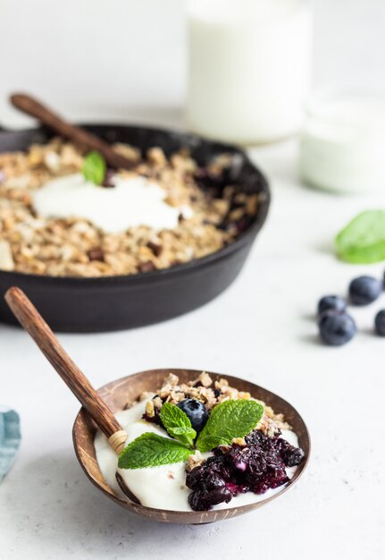 Oatmeal crumble in cast iron pan with fresh blueberry and natural yogurt.