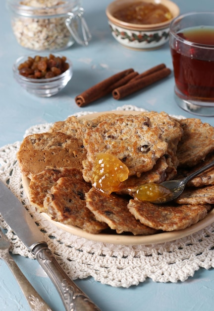 Oatmeal fritters with raisins are sprinkled with sweet syrup and served for breakfast with cup of tea and jam