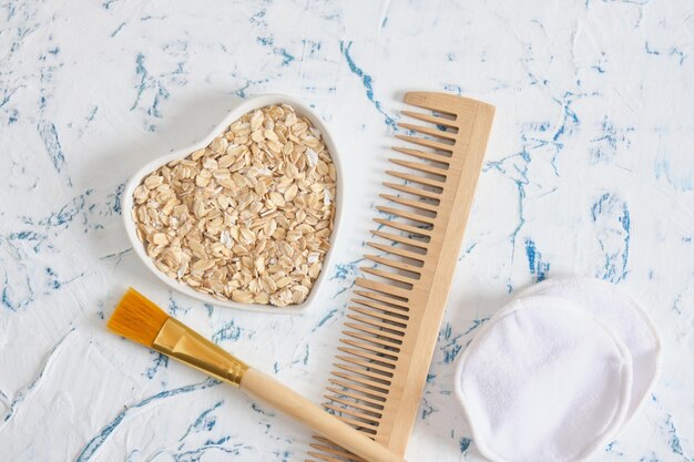 Oatmeal grains in a heartshaped bowl cotton pads comb and brush for applying the mask