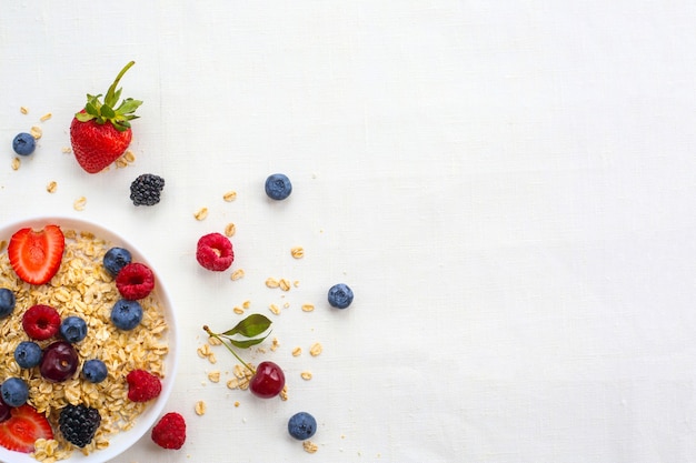 Oatmeal porridge in bowl topped with fresh berries, and homemade crunchy granola on white background