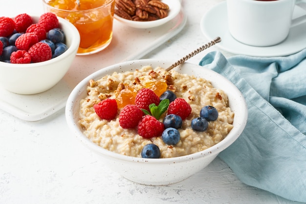 Oatmeal porridge with blueberry, raspberries, jam, side view, close up. Healthy diet