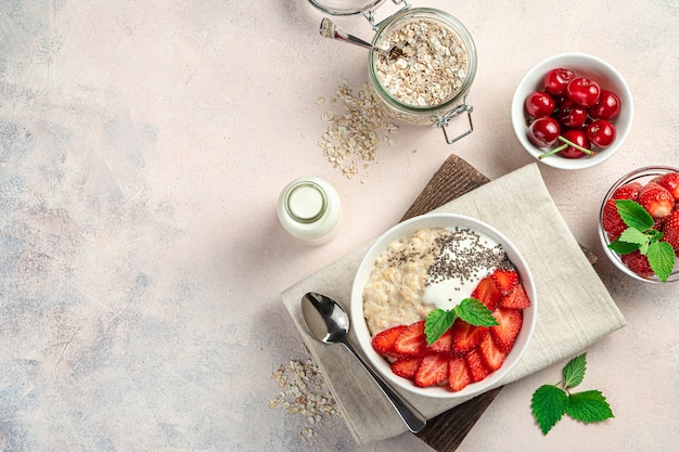 Oatmeal porridge with fresh berries and chia seeds on a light pink background with ingredients