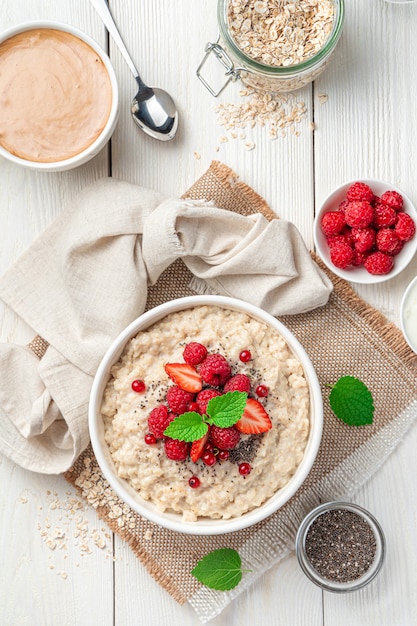 Oatmeal porridge with fresh raspberries strawberries and red currants on a white background